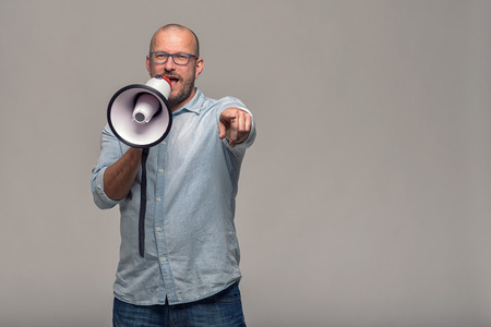 Man speaking over a megaphone as he makes a public address, participates in a protest or organises a rally or promotion, over grey with copy space to the sideの写真素材
