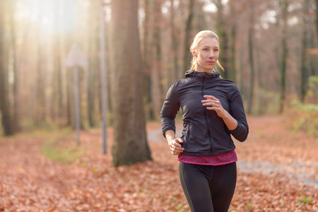 Pretty fit young woman jogging through autumn or fall woodland approaching the camera, close up...