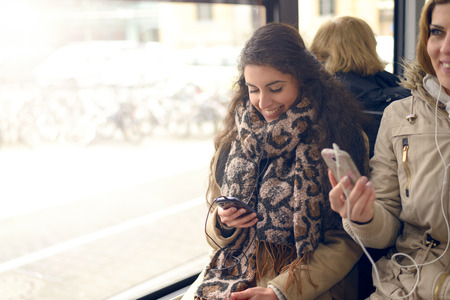 Happy brunette woman reading a message on her mobile phone while sitting in a bus, public transport and technology conceptの写真素材