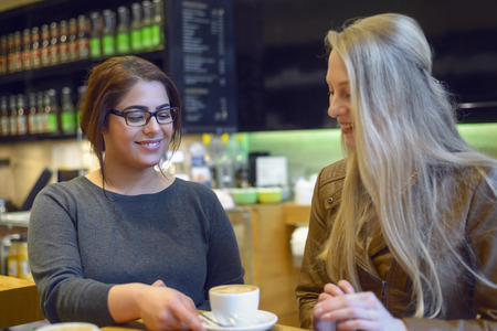 Young waitress serving a cup of coffee to a pretty young female customer in a restaurant or pub placing the cup on the table with a smileの写真素材