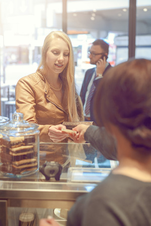 View over the shoulder of the cashier of an attractive young blond woman making payment at a till looking in her purseの写真素材