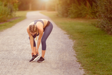 Young woman limbering up before training doing exercises to stretch her muscles on a country path in...