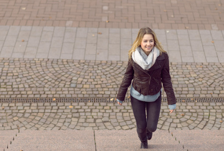 Smiling trendy young woman walking up steps outdoors with copyspaceの写真素材