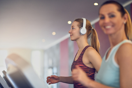 Attractive young woman with wireless headphones standing on treadmill in the gym, side view and smiling with copy spaceの写真素材