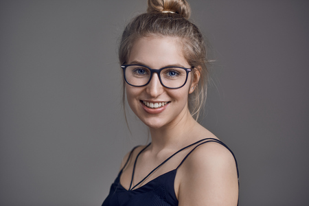 Attractive stylish blond woman with her hair in a bun wearing glasses smiling at the cameraの写真素材