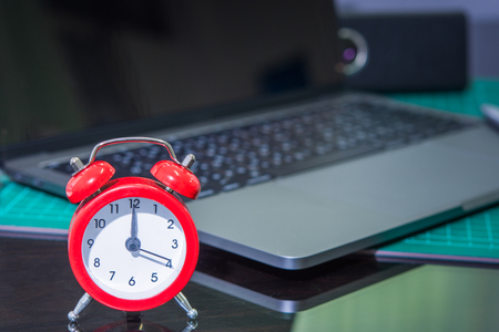 red clock on the desk and blur laptop backgroundの写真素材