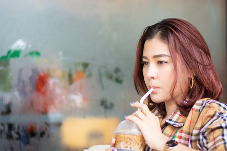 asia women sucking tube ice coffee in plastic glassの写真素材