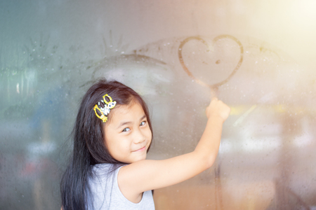 asia little girl writing heart on glassの写真素材