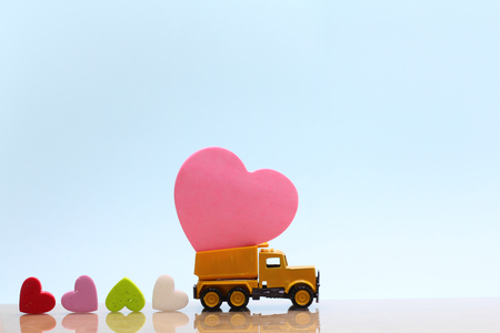 Yellow toy truck carry pink heart and many colorful hearts on back on pink background. Happy valentine's day and love conceptの写真素材
