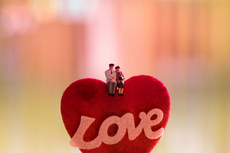 Miniature people: old couple in love sitting on red heart sign with word love on colorful light background. Happy valentine's day and love conceptの写真素材