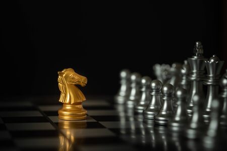 Gold knight chess stands on chessboard in front of opponents on dark background with copy space. Business strategy, planning, decision, and competition concept.の写真素材