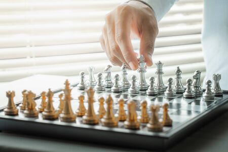Hand moving white king chess on chessboard game represent to business strategy, planning, decision making, and competition concept. Hobby and leisure.の写真素材