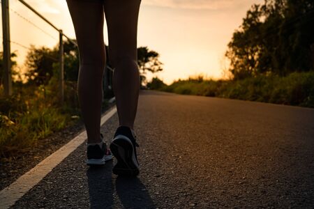 Silhouette back side view of young woman running on the road. Jogging in morning.の写真素材