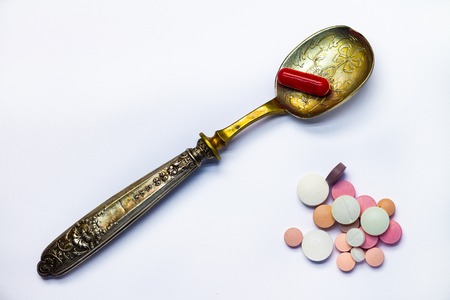 Drugs consumed orally. Colorful pills on a white background. A red capsule on an old spoon.の写真素材