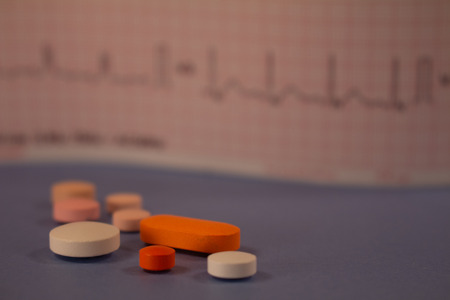 Pills of colors in a neutral background. Medications in the form of tablets. Electrocardiogram strip out of focus.の写真素材
