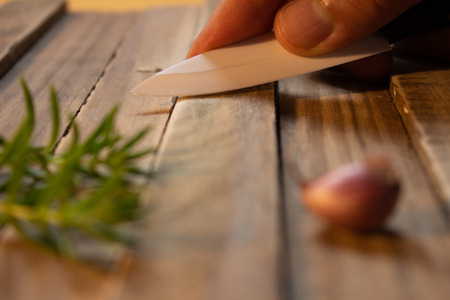 Garlic clove on a wooden rustic board. Ceramic knife held by a man. Some branches of rosemary.