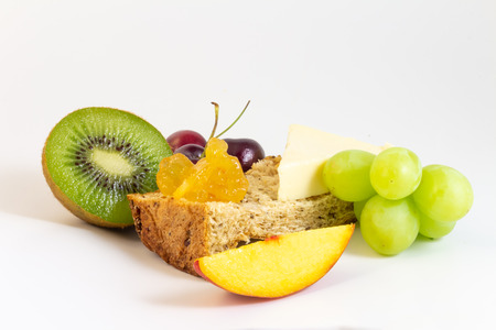 Fresh fruits for breakfast, wholemeal bread, cheese, peach, cherries, kiwi, grapes, etc. on white background.の写真素材