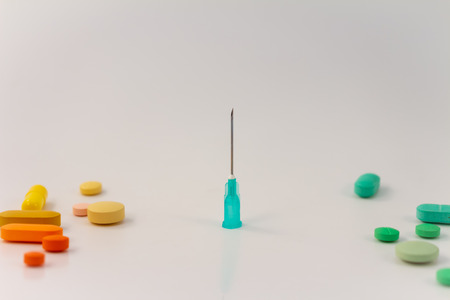 Some colored pills next to a metal needle. Addiction concept