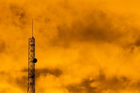 Antenna of communications between clouds of fire. The sky tinged with orange by the flames.の写真素材