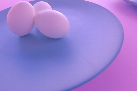 A light blue neutral plate with white chicken eggs on a neutral pink background. Free space to write. Organic and natural food.の写真素材