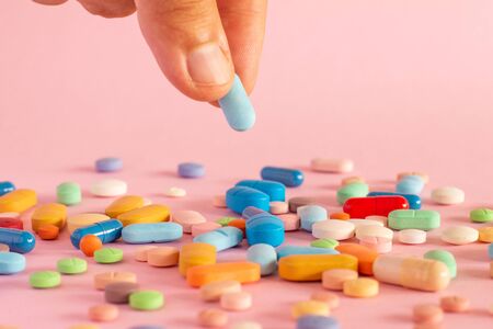 Man's hand holding a medicine. Colored pills on a neutral pink background. Prescription drugs for legal use.の写真素材