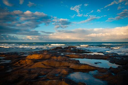 Coastal rocky landscape. Rocks at the edge of the sea. Beautiful clouds in the sky.の写真素材