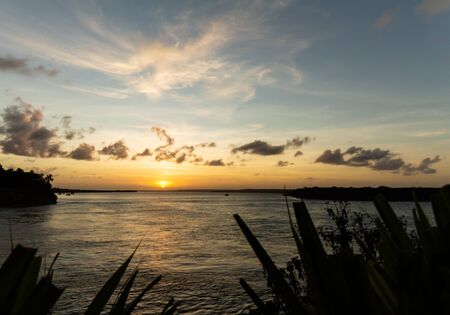 Sunset in the lagoon. The sun is hidden behind the clouds. Golden clouds in the sky. The water reflects the golden light of the sun.の写真素材