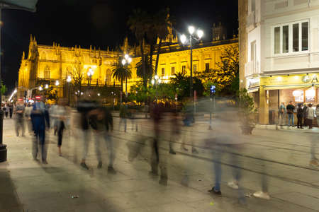 Sevilla Spain. April 27, 2018. Night view of the center of Seville. Passers blurred as ghosts. The illuminated cathedral stands out among the neighboring shops. Long exposure photography. Selective focus.のeditorial素材