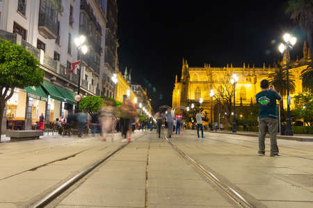 Sevilla Spain. April 27, 2018. Night view of the center of Seville. Passers blurred as ghosts. The illuminated cathedral stands out among the neighboring shops. Long exposure photography. Selective focus.のeditorial素材