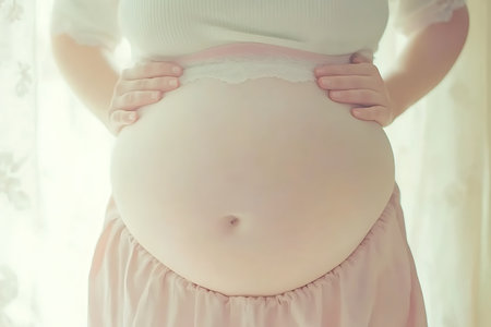 Close up of pregnant woman touching her belly with hands in light roomの素材