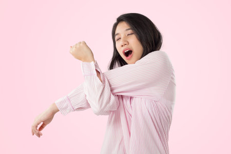 young asian woman wear pink pajamas yawn and stretch when her wake up feeling sleepyの写真素材