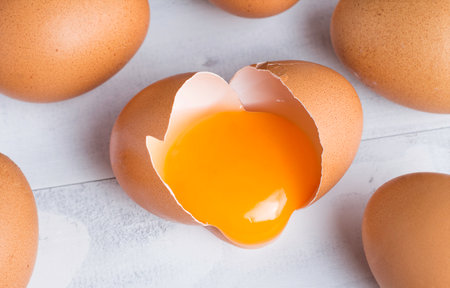 raw broken chicken egg , egg yolk in shell on white woodenの写真素材