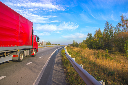 Red truck moving on a highway at bright sky
