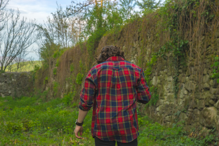 Serious young handsome man in checkered shirt bent down near castle wallの写真素材