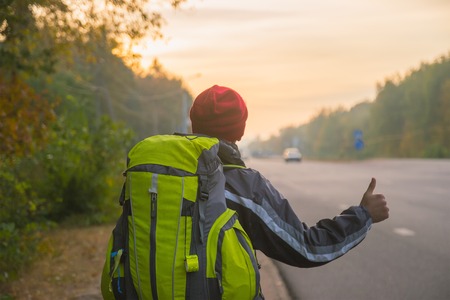 Hitchhiking young traveller try to catch car in the morningの写真素材