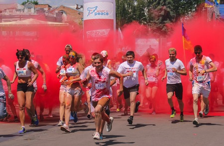 Zhytomyr, Ukraine - June 25, 2016: happy people crowd partying under colorful powder cloud at holi...