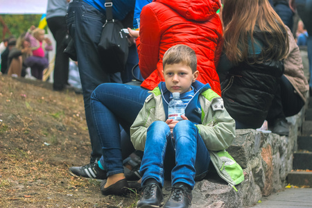 Zhytomyr, Ukraine - September 05, 2015: sad teen sit on the ground by holding bottle in hands at crowdのeditorial素材