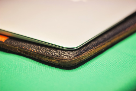part of the gray laptop lies on a leather cover on a green table