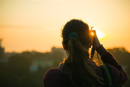 Silhouette of a girl taking pictures of the sunriseの写真素材