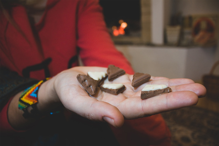 Christmas tree chocolate shapes in girl hands at fireplace background