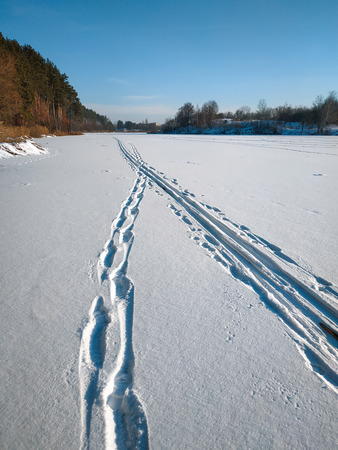 Human traces and animals in the snow at frozen riverの写真素材