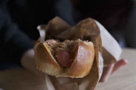 Fresh hot dog with grilled sausage, served outdoors. Cookout american bbq food. Hot-dog with meat and vegetables salad filling closeup in chef's hands. Street food, fast food.の写真素材