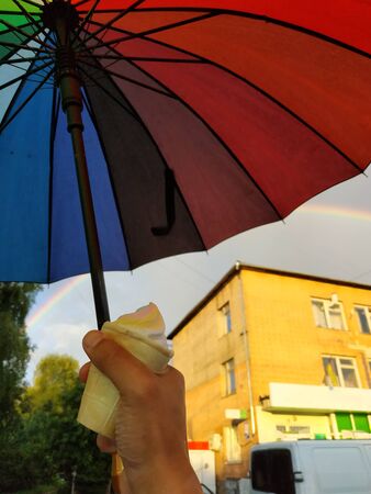 girl hand holding ice cream, weather and umbrella of rainbow coloursの写真素材