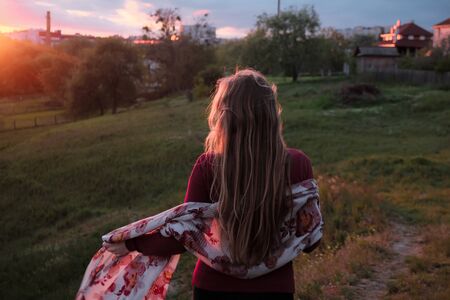 Stylish young girl back on a hill in the forest admiring the sunset. A girl with a plaid. Enjoy the sunset and the view. faceless, rear viewの写真素材