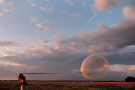 Silhouette of female hand holding balloon with hearts against sundown purple sky.