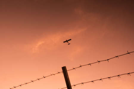 Orange hanging curtains of smoke from a large wildfire and obscuring a firefighting plane in the sky at fence background.の写真素材