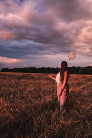 Silhouette of female holding balloon with hearts against sundown purple sky at wheat fieldの写真素材