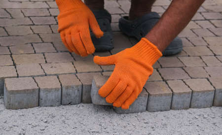 Construction worker installing and laying pavement stones on terrace, road or sidewalk. Worker using stones to build sidewalkのeditorial素材