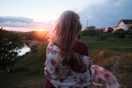 Stylish young girl back on a hill in the forest admiring the sunset. A girl with a plaid. Enjoy the sunset and the view. faceless, rear viewの写真素材