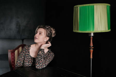 beautiful thoughtful woman sitting at dark room with green table lampの写真素材